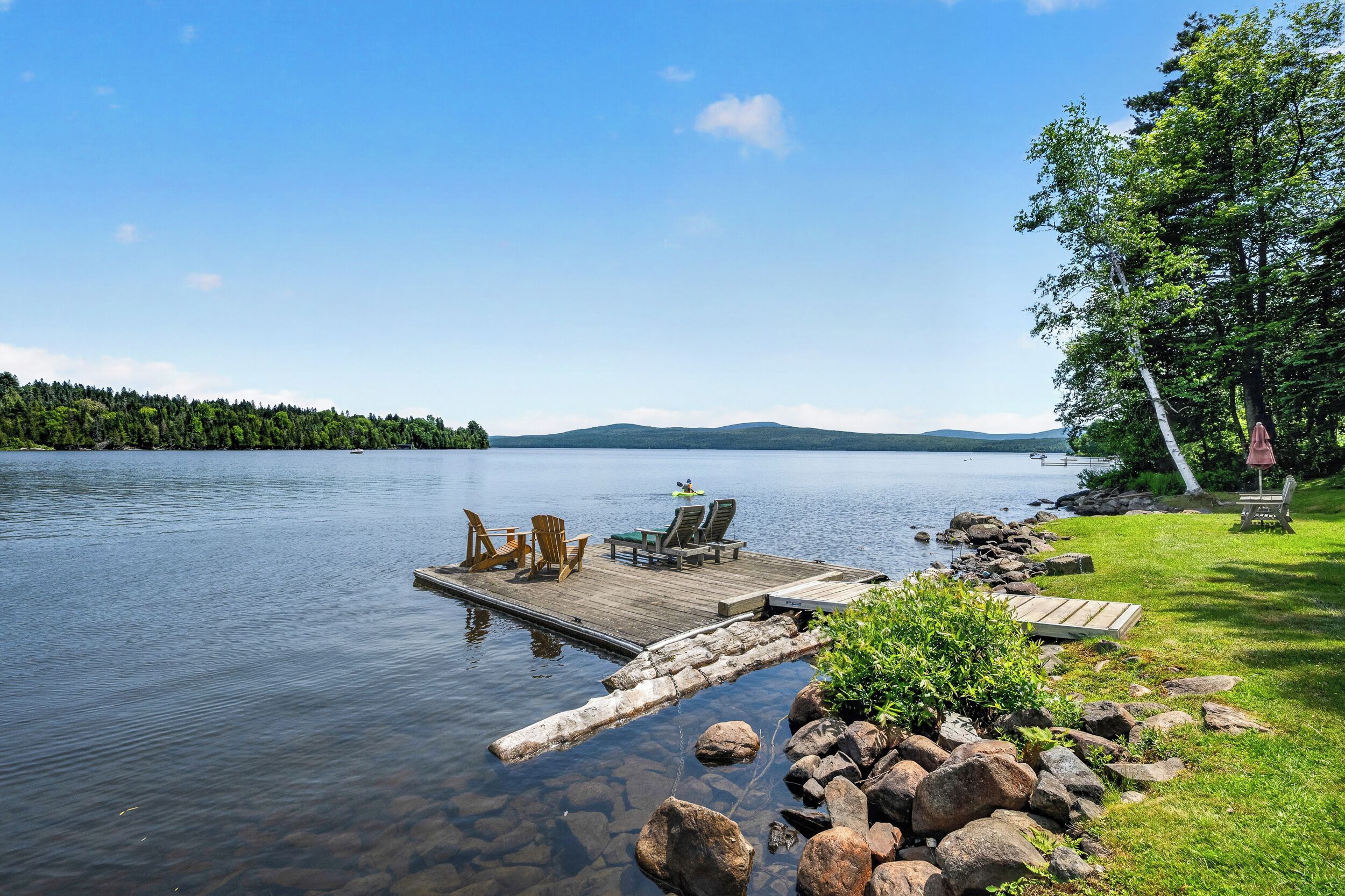 A calm lake with a wooden dock extending into the water, surrounded by rocks and greenery.