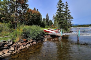 A serene lakeside setting with boats docked at a wooden pier, surrounded by lush greenery and trees. - Hunter Cove Cabin #4 in the Hunter Cove Cabins Community! (Rangeley)