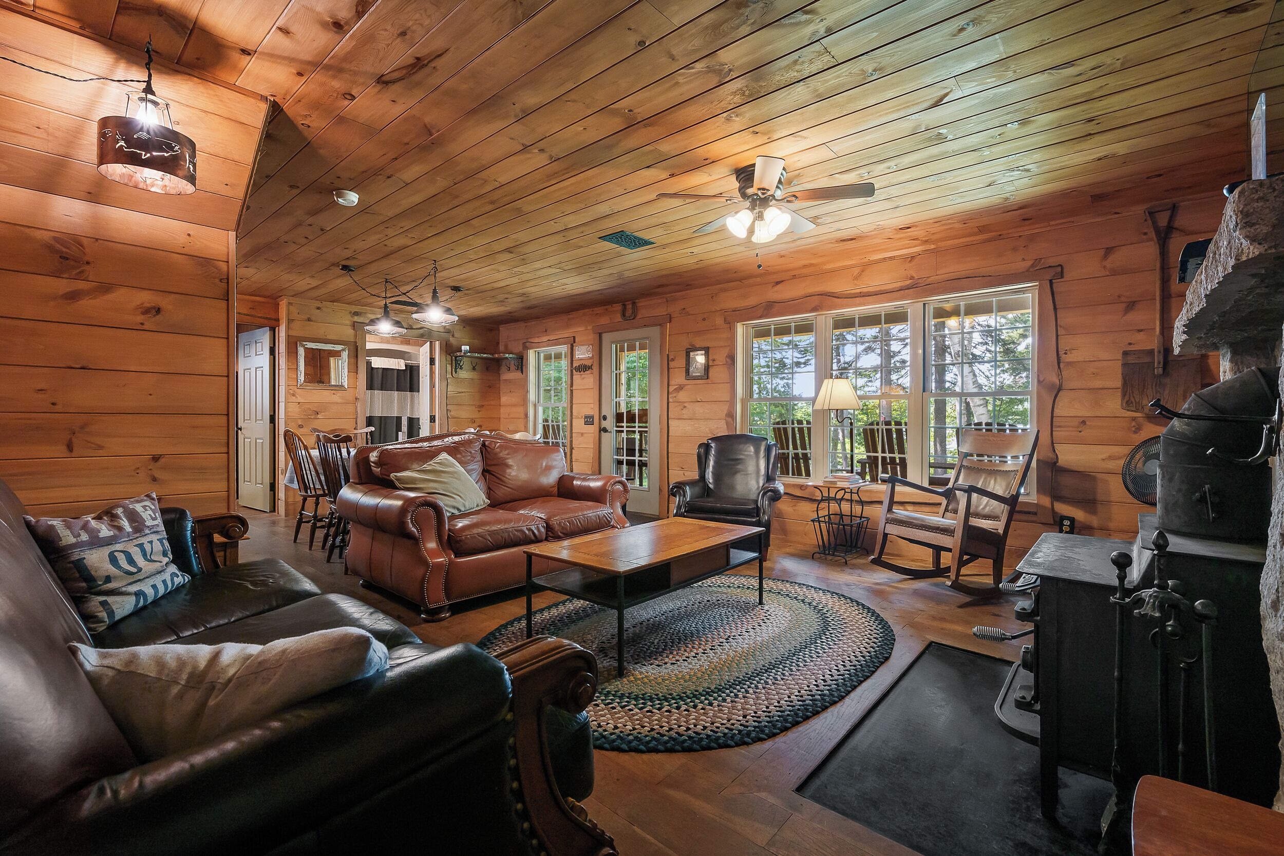 A cozy cabin interior with a wooden ceiling, leather furniture, and a fireplace.