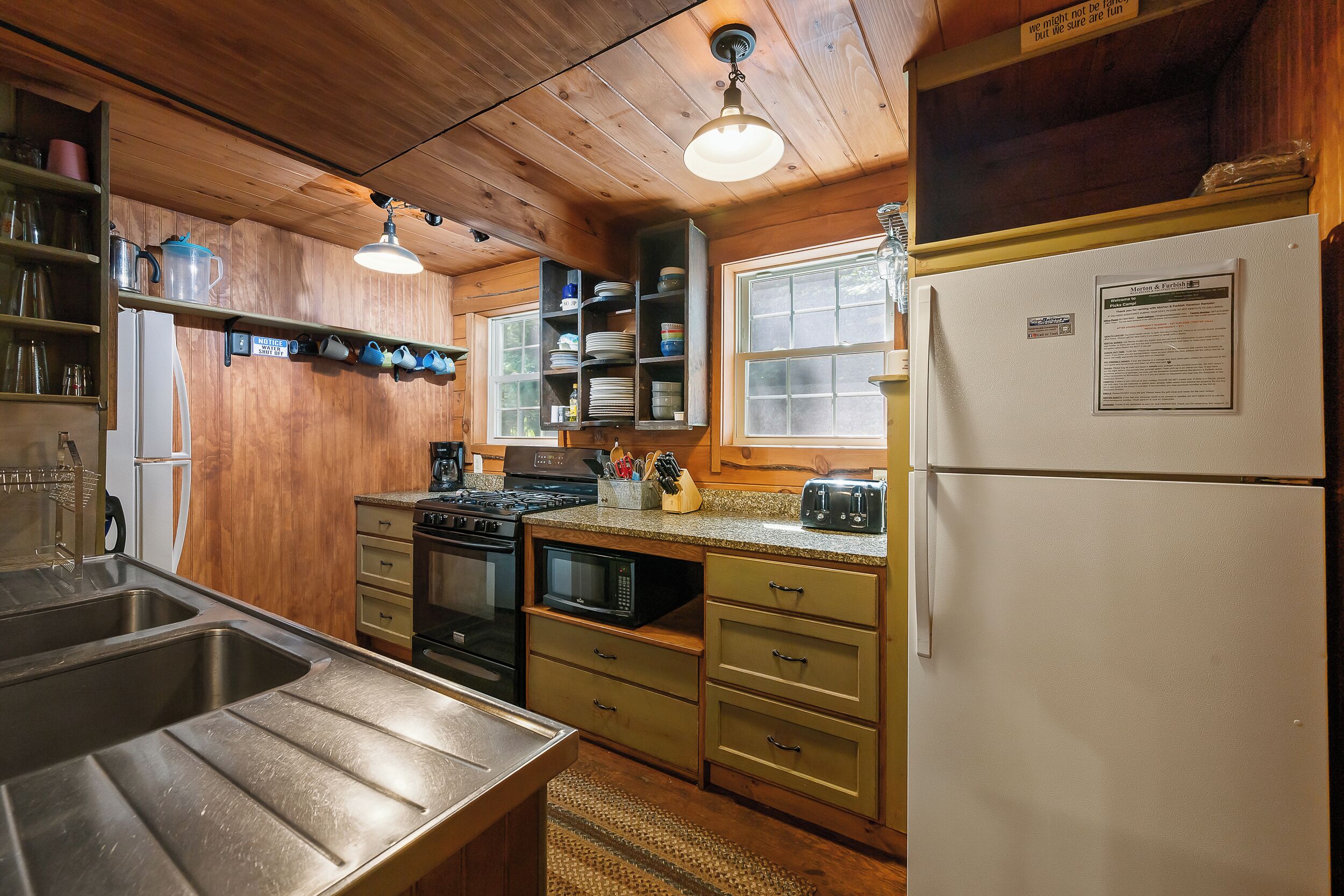 A kitchen with wooden cabinets, a stainless steel sink, a stove, and a refrigerator.