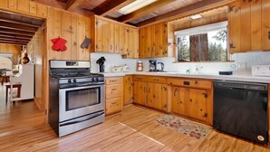 Une cuisine avec des meubles en bois, une cuisinière, un lave-vaisselle et une fenêtre donnant sur les arbres.