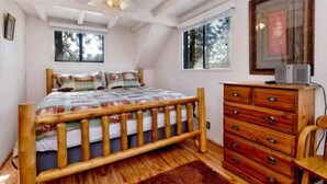 Une chambre à coucher avec un lit en bois, un ventilateur de plafond, une commode et une fenêtre donnant sur les arbres.