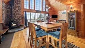 A cozy cabin interior with a stone fireplace, wooden dining table, and chairs. - 🐾Michaud Mountain Chalet - Private cabin with incredible views of Rangeley Lake! Dog Friendly (Rangeley)