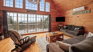 A cozy log cabin interior with a large window, a fireplace, and a sign reading "RANGELEY". - 🐾Michaud Mountain Chalet - Private cabin with incredible views of Rangeley Lake! Dog Friendly (Rangeley)