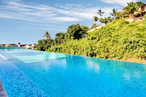 A clear blue infinity pool with a view of lush greenery and a distant building. - Hotel Puerto Sayulita (Sayulita)