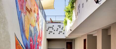 Un immeuble à plusieurs étages orné d’une fresque colorée sur le mur extérieur, doté d’un espace extérieur couvert agrémenté de plantes et d’un escalier reliant les différents étages.