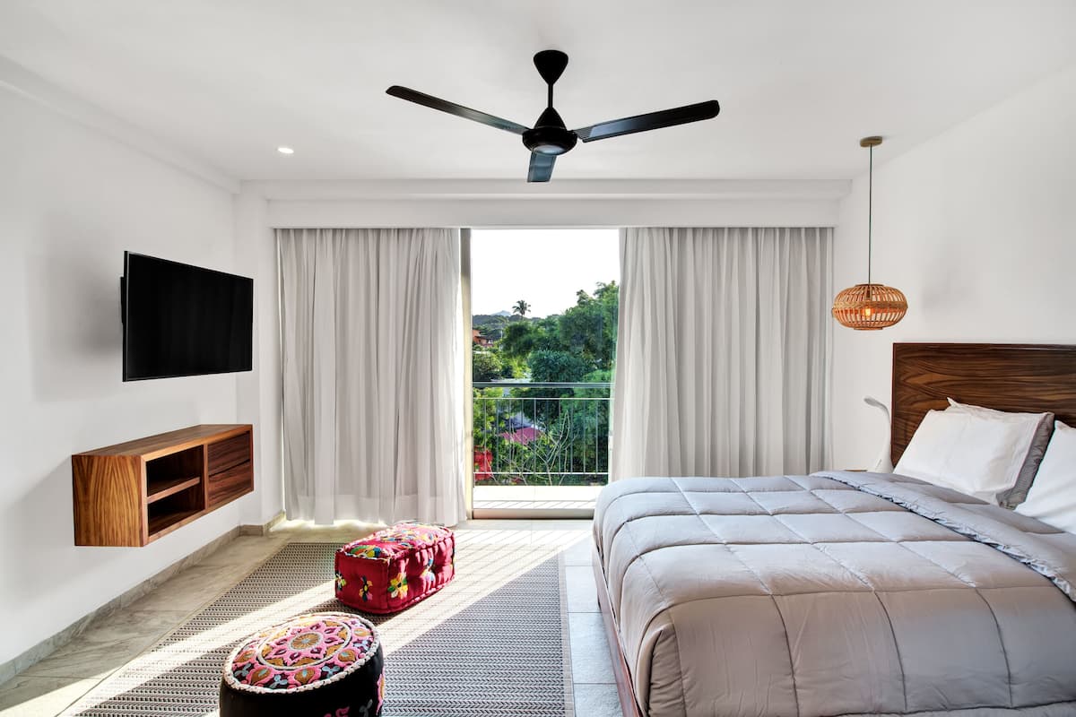 A modern hotel room with a bed, a ceiling fan, a TV, and a balcony with curtains.