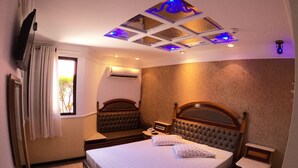 A hotel room with a large bed, a bedside table, a mirror, a TV mounted on the wall, and a ceiling with decorative lighting. - Motel Villa di Roma - Adults Only (Guarujá)