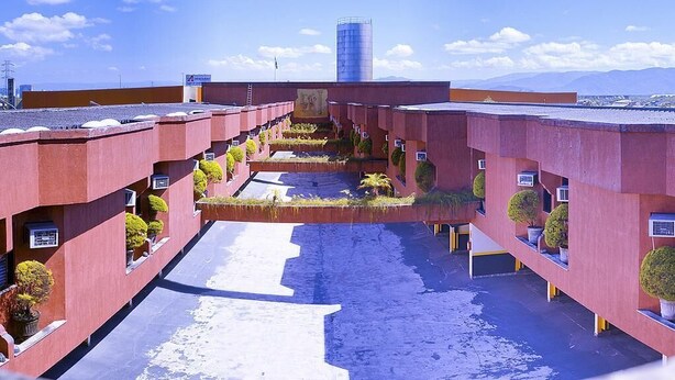 A multi-story hotel with a central courtyard, featuring balconies with potted plants and a view of distant mountains. - Motel Villa di Roma - Adults Only (Guarujá)