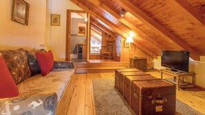 Une pièce mansardée chaleureuse avec un plafond en bois, un canapé agrémenté de coussins à motifs, une télévision et une cheminée.