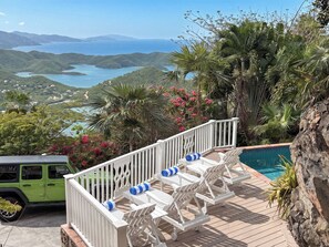 A deck with lounge chairs overlooking a pool and a view of a coastal landscape.
