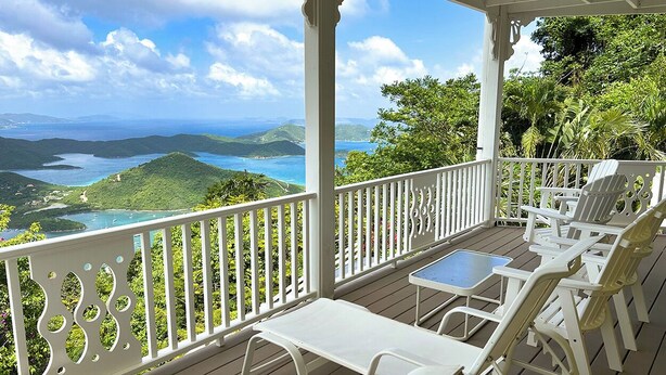 A covered outdoor seating area with white chairs and a table, overlooking a scenic landscape with hills and a body of water. - Experience the ultimate retreat at One Particular Harbour, where breathtaking views meet unparalleled privacy, creating the perfect oasis for relaxation and rejuvenation. This is the getaway you’ve been dreaming of! (Coral Bay)