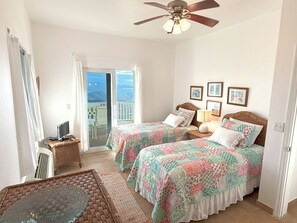 A bedroom with two beds, a ceiling fan, a small table, and a view of the outdoors. - Experience the ultimate retreat at One Particular Harbour, where breathtaking views meet unparalleled privacy, creating the perfect oasis for relaxation and rejuvenation. This is the getaway you’ve been dreaming of! (Coral Bay)