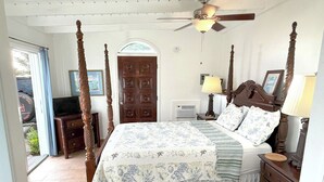 A four-poster bed with a floral bedspread, a wooden nightstand, a lamp, and a door with a window. - Experience the ultimate retreat at One Particular Harbour, where breathtaking views meet unparalleled privacy, creating the perfect oasis for relaxation and rejuvenation. This is the getaway you’ve been dreaming of! (Coral Bay)