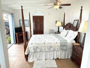 A four-poster bed with a floral bedspread, a wooden nightstand, a lamp, and a door with a window.