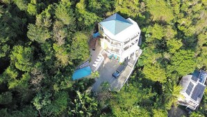 A two-story building with a blue roof, surrounded by dense greenery. - Experience the ultimate retreat at One Particular Harbour, where breathtaking views meet unparalleled privacy, creating the perfect oasis for relaxation and rejuvenation. This is the getaway you’ve been dreaming of! (Coral Bay)