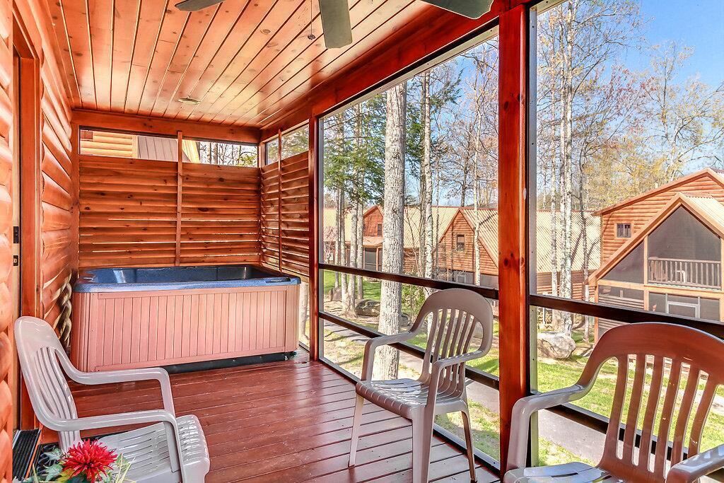 A wooden cabin with a hot tub, two chairs, and a view of other cabins.