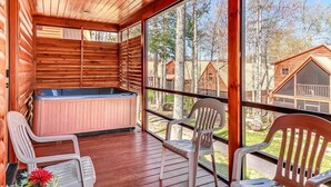 Eine Holzhütte mit Whirlpool, zwei Stühlen und einem großen Fenster mit Blick auf einen Wald.