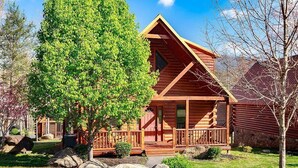 Eine Blockhütte mit Veranda, umgeben von einem gepflegten Rasen und großen Steinen.