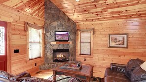 Ein rustikales Blockhaus-Interieur mit Kamin aus Stein, Ledersofas und einem Fernseher.