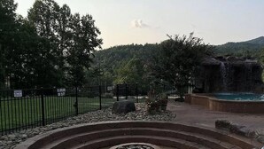 Ein angelegter Außenbereich mit einem runden Steinbrunnen, einem eingezäunten Garten und einem Wasserfall.