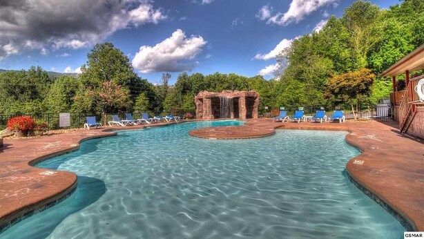 Ein Swimmingpool mit Wasserfall, umgeben von Liegestühlen und einer Holzterrasse.