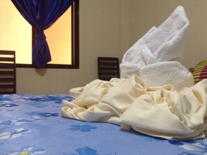 Un lit avec une couvre-lit à motifs floraux, une serviette blanche et un rideau bleu.