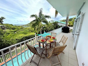 A balcony with a pool, wooden chairs, and a table set for dining.