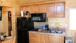A compact kitchen with wooden cabinets, a black refrigerator, a microwave, and a sink.