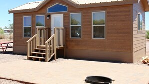 A small wooden cabin with a porch, a set of stairs, and a clear sky.