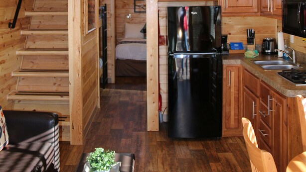 A wooden cabin interior with a kitchen, dining area, and a loft bedroom.