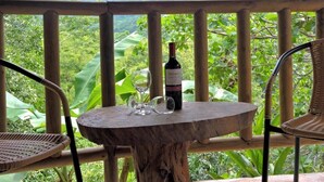 A wooden table with a bottle and glasses on a balcony with a view of a mountain and lush greenery. - Hostal Restaurante y Spa Mama Neyumun (Santa Marta)