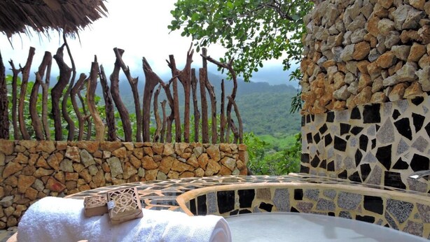 A hot tub area with a stone wall, wooden branches, and a view of a lush landscape. - Hostal Restaurante y Spa Mama Neyumun (Santa Marta)