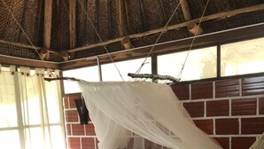 A bed with a mosquito net, a brick wall, and a window with curtains. - Hostal Restaurante y Spa Mama Neyumun (Santa Marta)
