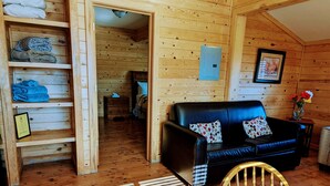 A cozy wooden cabin interior with a black leather sofa, wooden shelves, and a dining area with a table and chairs. - Kingman KOA (Kingman)