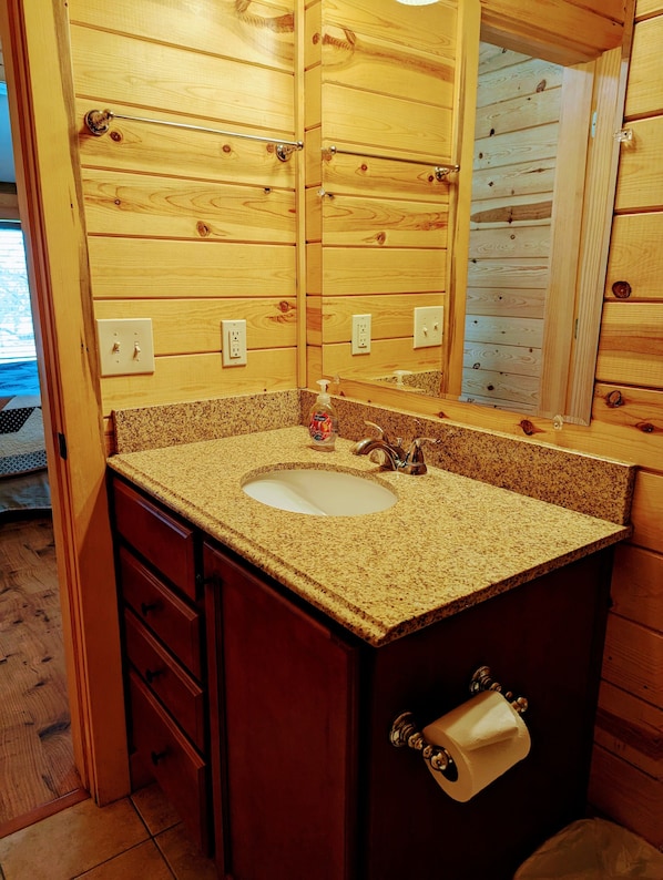 A wooden bathroom with a granite countertop sink, a mirror, and a toilet paper holder. - Kingman KOA (Kingman)