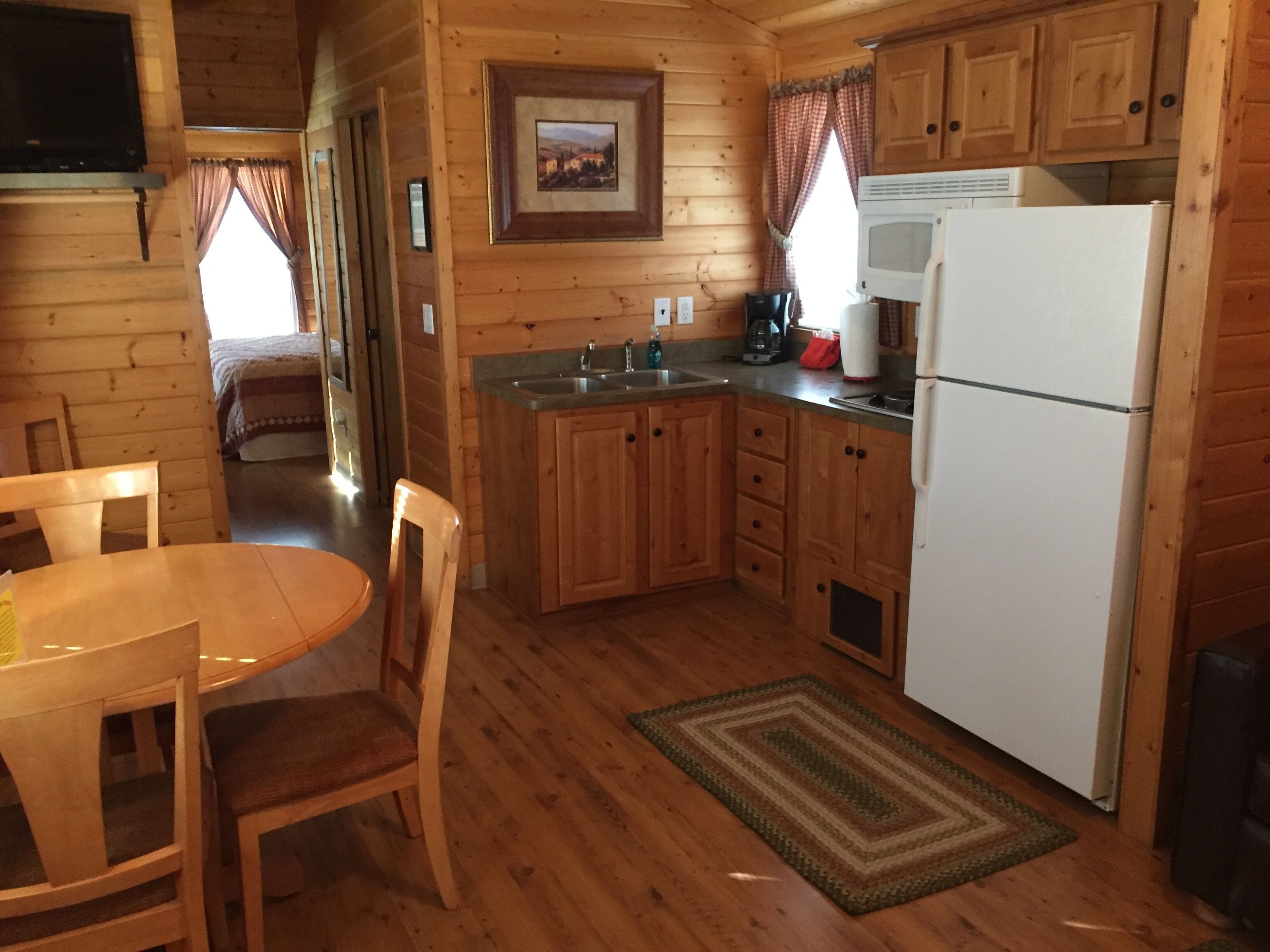 A wooden cabin interior with a kitchen area, a dining table, and chairs.