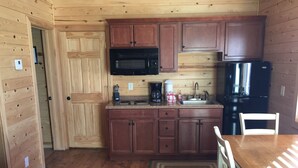 A compact kitchen with wooden cabinets, a microwave, a stove, a sink, and a refrigerator. - Kingman KOA (Kingman)