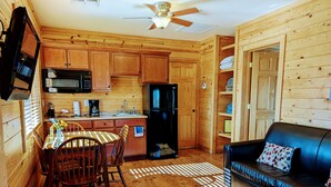 A cozy cabin-style kitchen with wooden cabinets, a black refrigerator, and a dining area with a table and chairs. - Kingman KOA (Kingman)