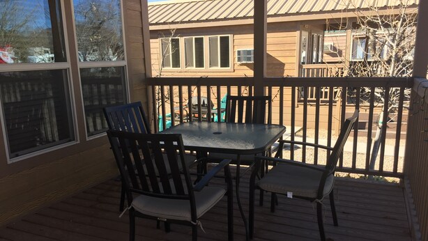 A covered patio with a table and chairs, a railing, and a view of a building in the background. - Kingman KOA (Kingman)
