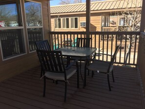 A covered patio with a table and chairs, a railing, and a view of a building in the background. - Kingman KOA (Kingman)