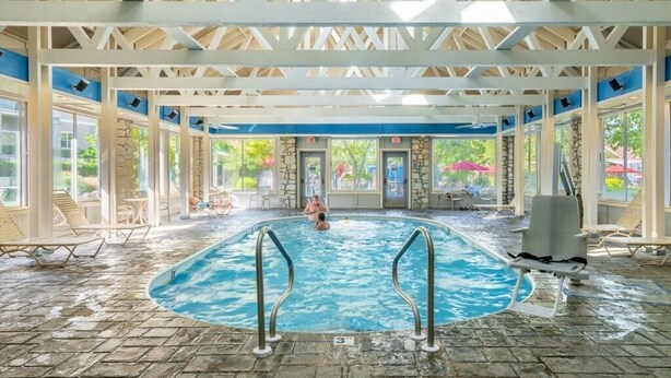 Una piscina interior con agua cristalina, rodeada de sillones de descanso y una zona cubierta con una pared de piedra.