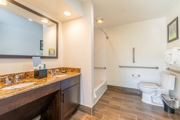 A modern bathroom with a granite countertop, a large mirror, a shower, and a toilet.