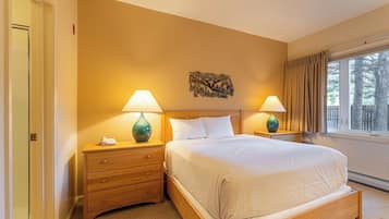 A hotel room with a bed, two bedside tables with lamps, a wooden headboard, a wall-mounted artwork, and a window with curtains.