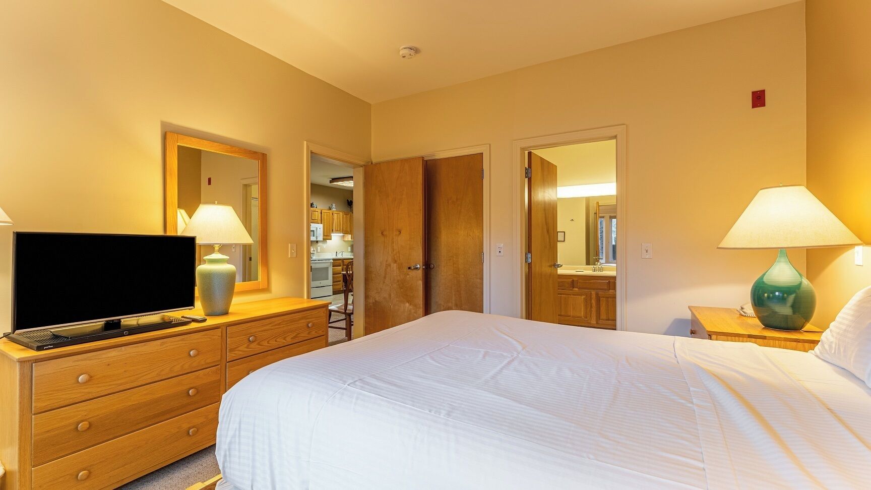 Une chambre d’hôtel avec un lit, un téléviseur posé sur une commode en bois, une lampe et un miroir.