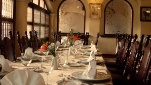 Una mesa de comedor formal cubierta con manteles blancos, platos y copas, flanqueada por sillas de madera.