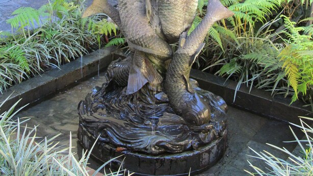 Una estatua de bronce de una sirena con cola de pez, sobre una base circular rodeada de agua.