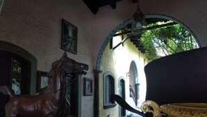 Una habitación con una estatua de caballo, un jarrón grande y vistas a un espacio exterior con arcos y vegetación.