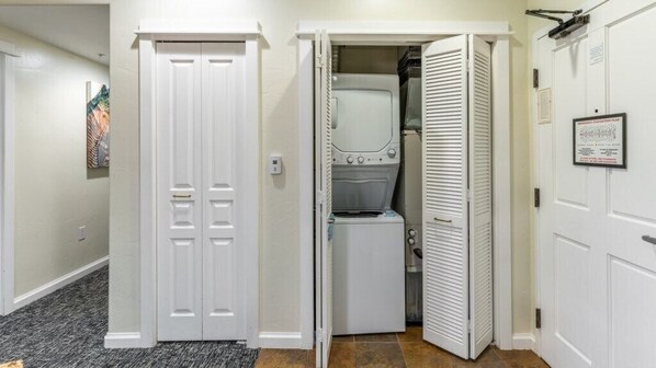Un pasillo con una puerta blanca cerrada, un área de lavandería con lavadora y secadora, y un armario blanco cerrado.