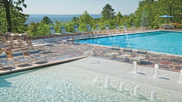 A pool area with clear water, lounge chairs, and a view of trees and mountains in the background. - Wyndham Resort At Fairfield Bay - 1 Bedroom Deluxe (Fairfield Bay)